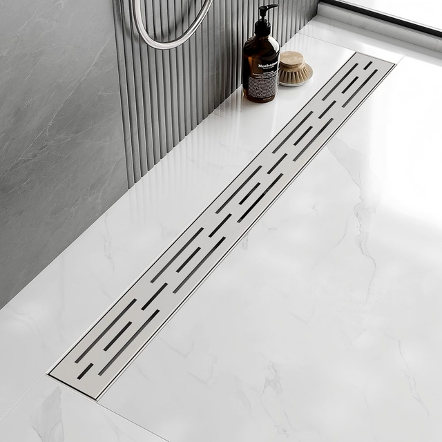 Stainless steel linear drains for shower installed flush in a white marble bathroom floor
